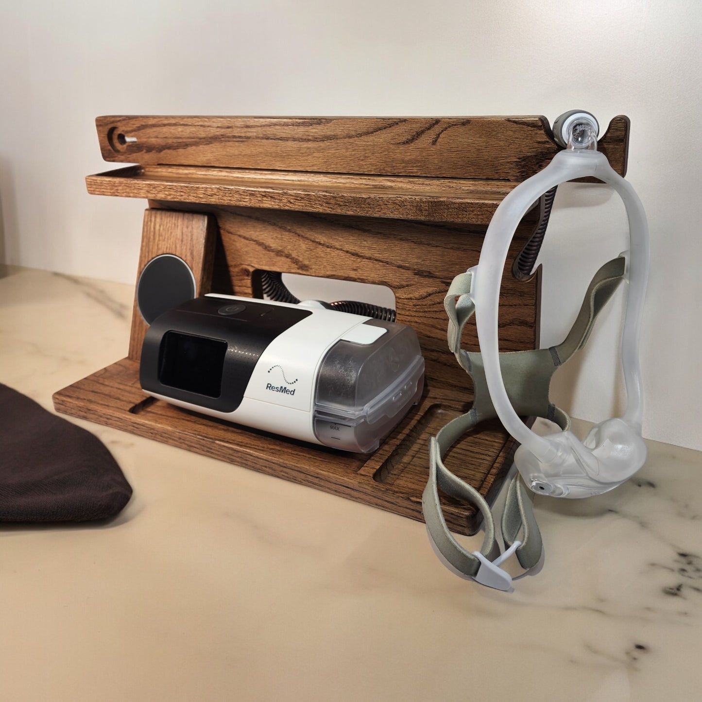 A CPAP Smart Stand that has the CPAP inserted and mask hanging from the stand. This stand also includes the optional wireless phone charger.