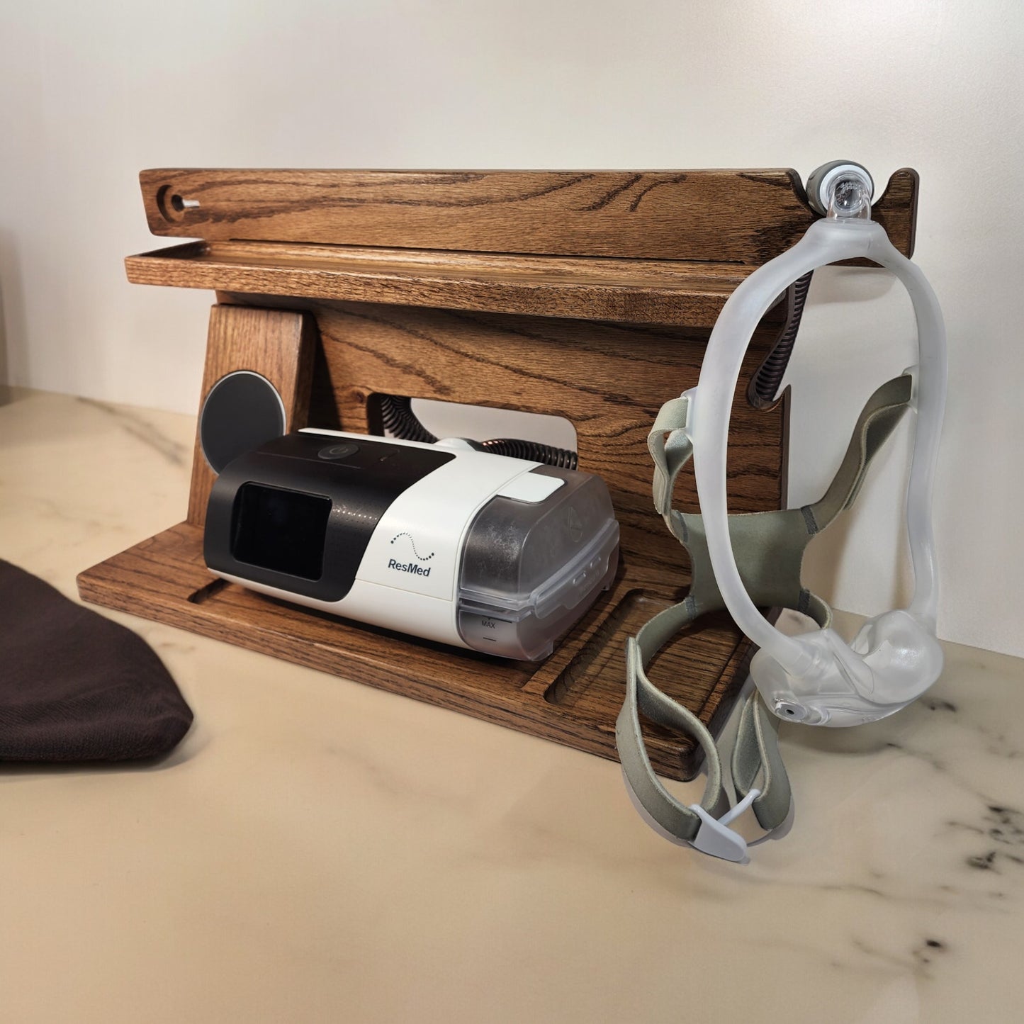 A CPAP Smart Stand that has the CPAP inserted and mask hanging from the stand. This stand also includes the optional wireless phone charger.