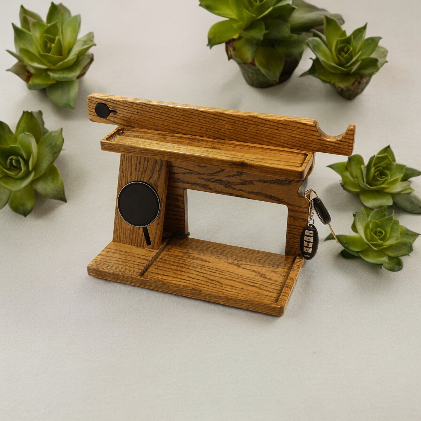 An empty CPAP Smart Stand made by Custom Cave Works. This smart stand does include the optional wireless phone charger. The stand is on a white background and includes places to put your smartphone, smartwatch, change, keys and wallet. The stand is sold oak wood that has a satin finish.