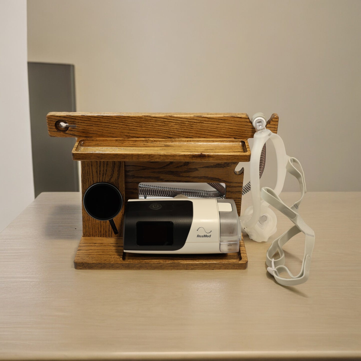 A CPAP Smart Stand that has the CPAP inserted and mask hanging from the stand. This stand also includes the optional wireless phone charger.