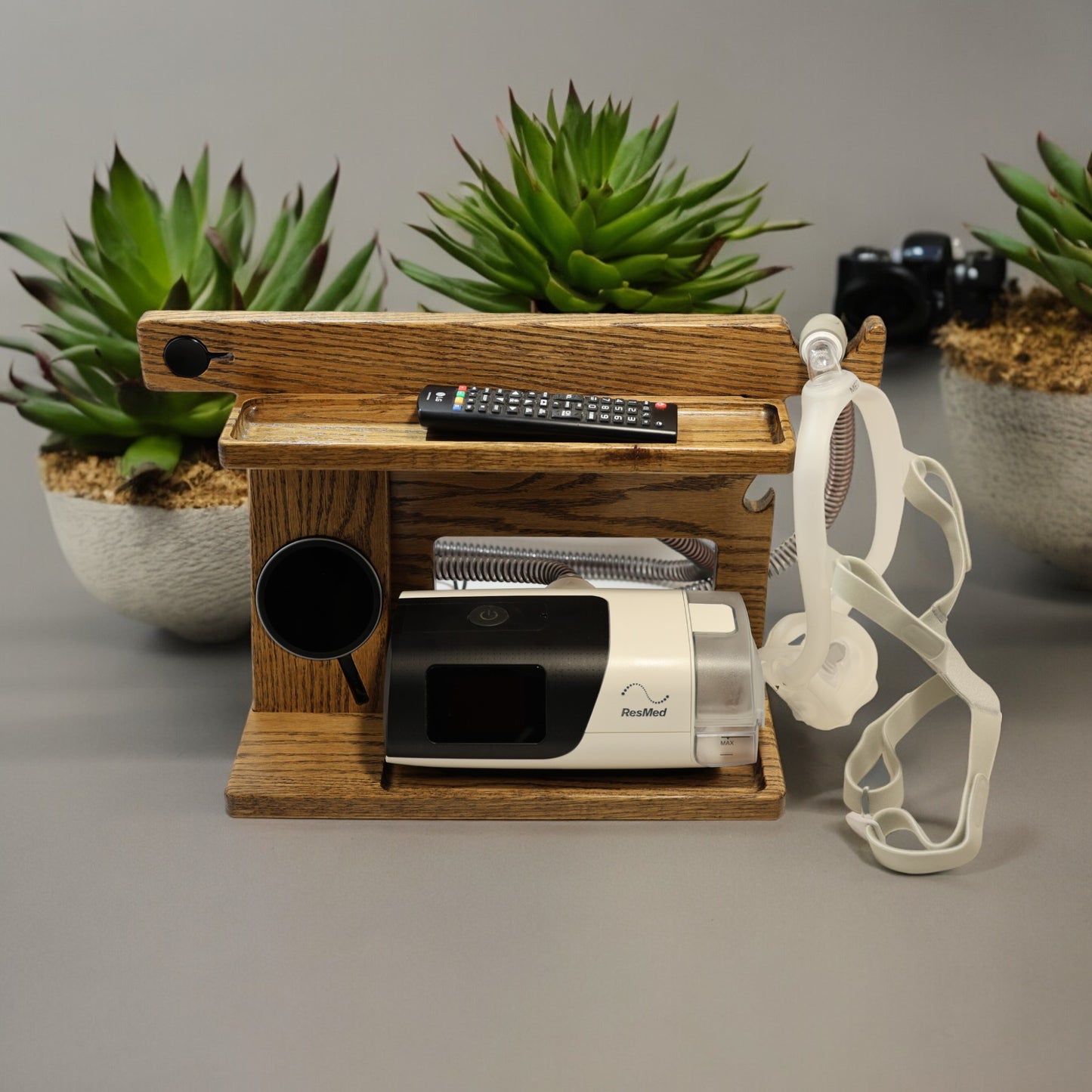 A CPAP Smart Stand that has the CPAP inserted and mask hanging from the stand. This stand also includes the optional wireless phone charger.